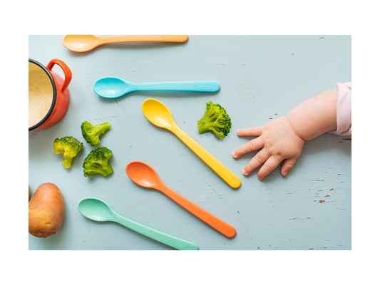 A baby grabbing a spoon before he starts to eat his solid foods like broccoli.