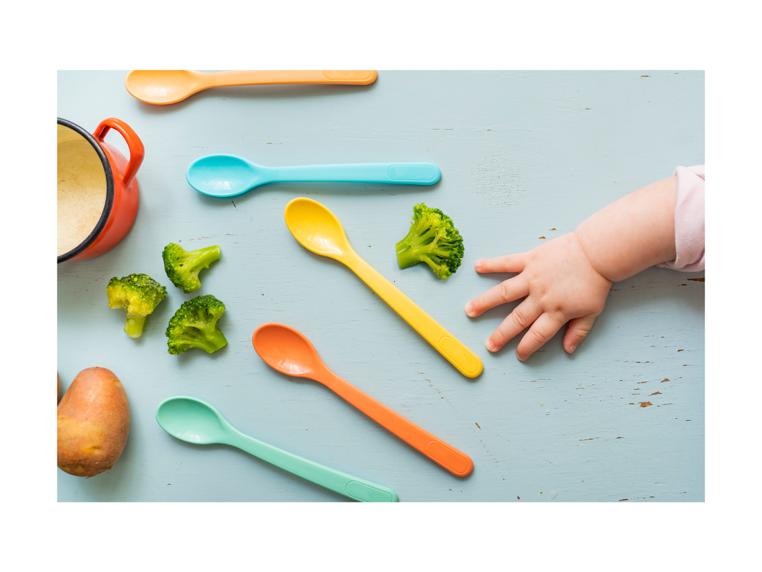 A baby grabbing a spoon before he starts to eat his solid foods like broccoli. 